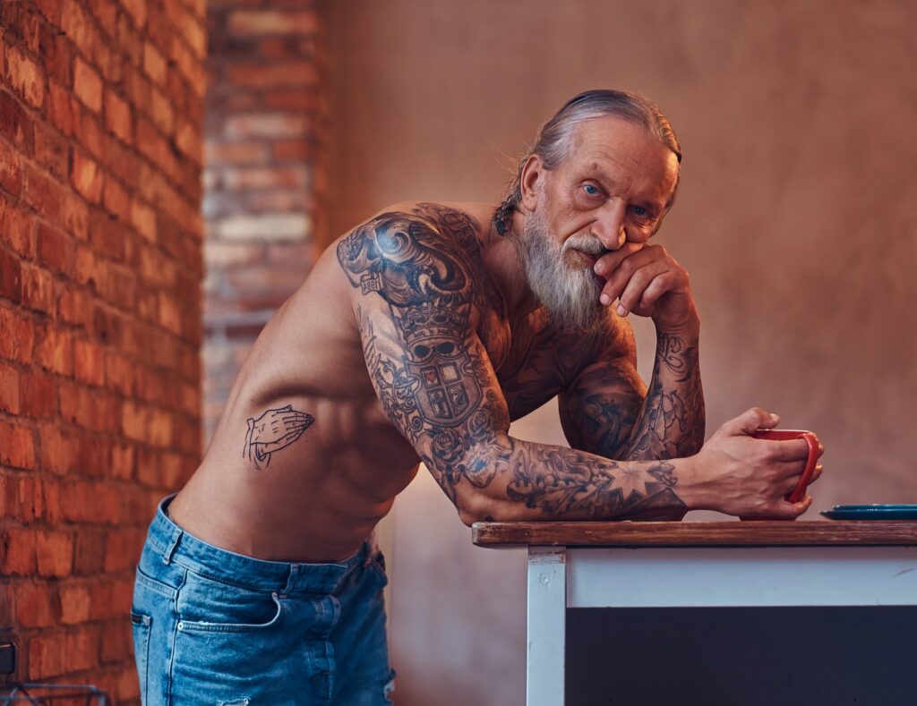 Muscular elderly man with tattooed body indoors room